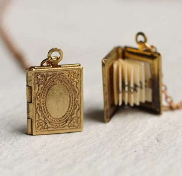 A close up of a gold necklace charm in the shape of a book